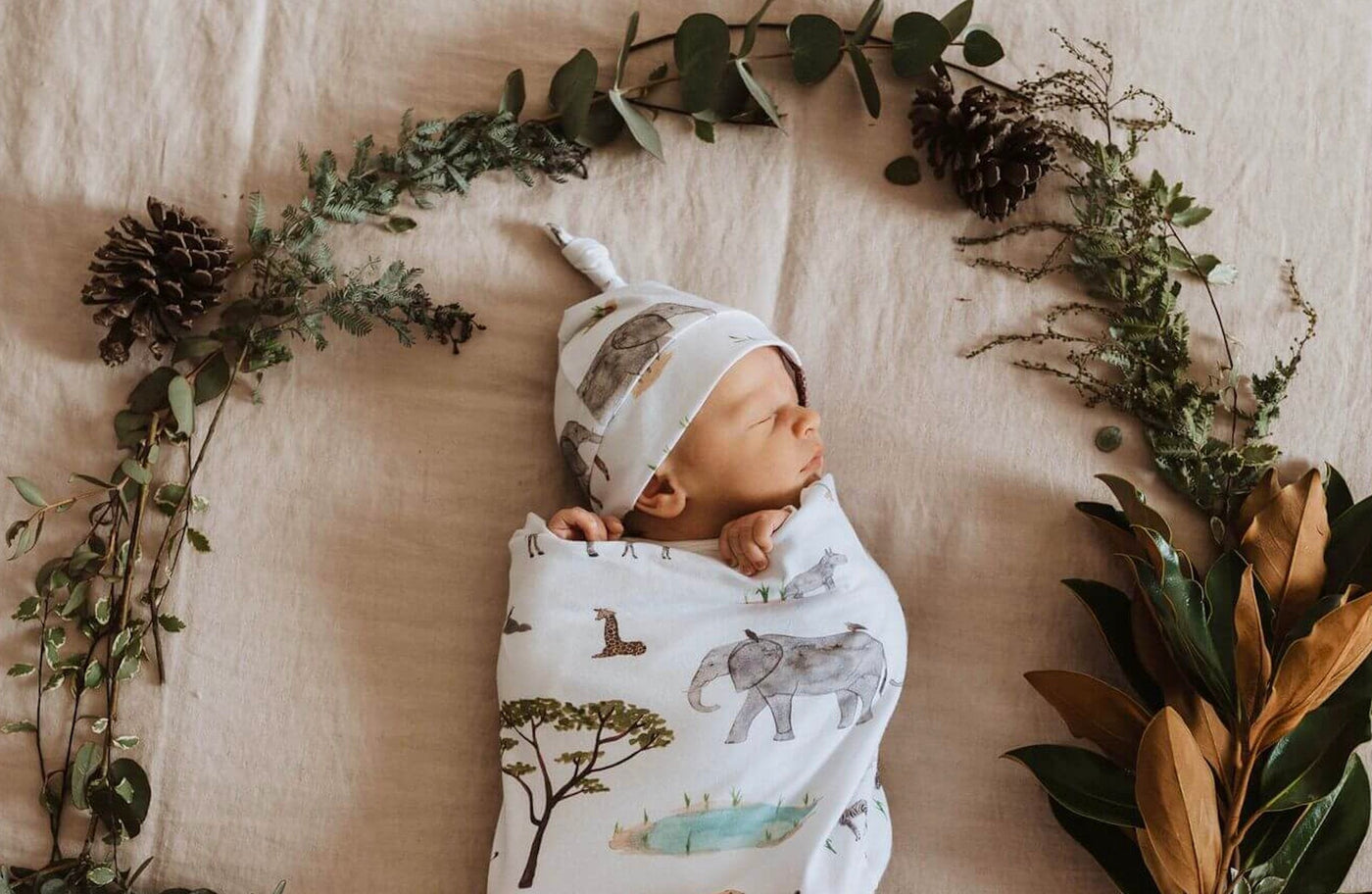 A child comfortably resting with a Snuggle Swaddle & Beanie Set, beautifully decorated with wild animals like giraffes, hippos, and elephants.